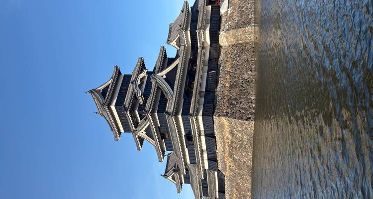 Le château de Matsumoto au toit sombre s'élève au-dessus de sa base de pierre et de ses douves contre un ciel bleu clair.
