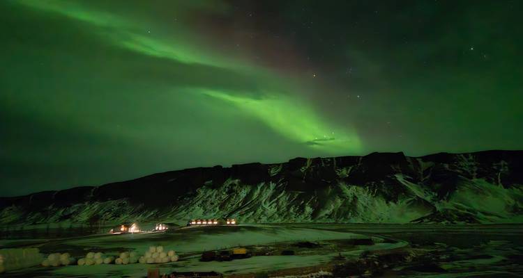 Une brillante aurore boréale verte danse au-dessus des montagnes islandaises enneigées et des lumières de la ferme