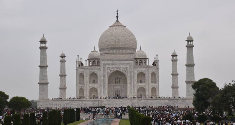 Vue de face du Taj Mahal avec de grandes foules rassemblées le long du bassin de réflexion par temps nuageux.