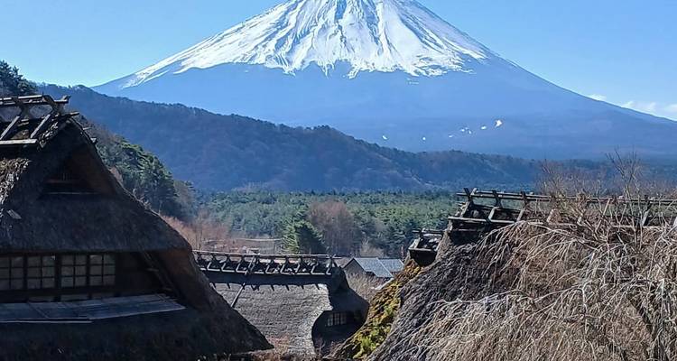 Traditional thatched village houses lie beneath the majestic snowy cone of Mount Fuji on a clear day.