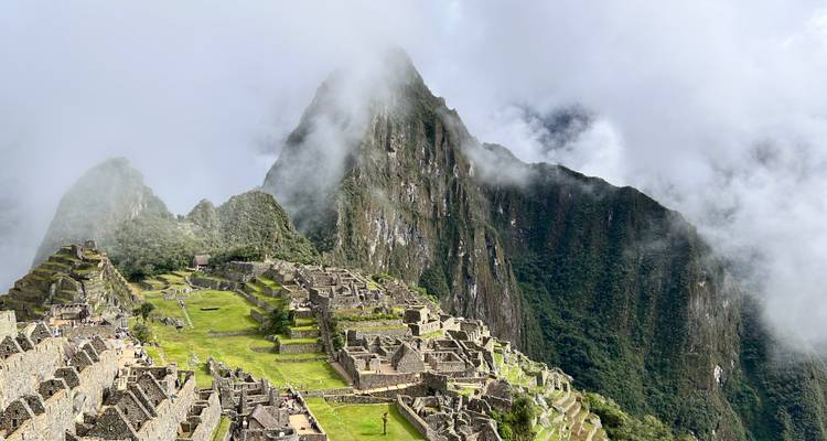 Iconic panoramic view of Machu Picchu ruins perched on a green mountain ridge with clouds drifting around steep peaks.