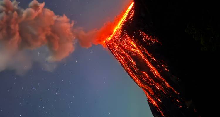 Larga exposición nocturna de un volcán en erupción con ríos de lava incandescente y una columna de ceniza bajo un cielo estrellado.