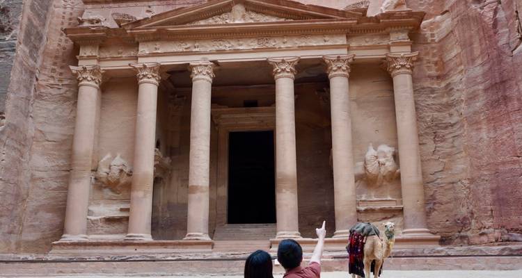 Visitantes y un camello frente a la icónica fachada del Tesoro tallada en acantilados de color rojo rosado en Petra.