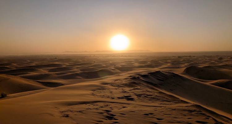 Weite goldene Sanddünen, die sich bis zum Horizont erstrecken unter einer glühenden untergehenden Sonne.