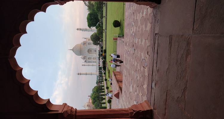 De Taj Mahal omlijst door een rood zandstenen boog met bezoekers die over de binnenplaats lopen in de schemering.