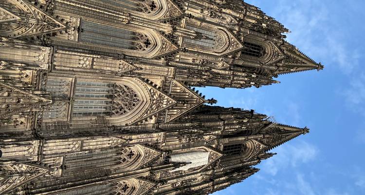 Dramatische Froschperspektive der Zwillingstürme und der verzierten Fassade des Kölner Doms vor blauem Himmel.