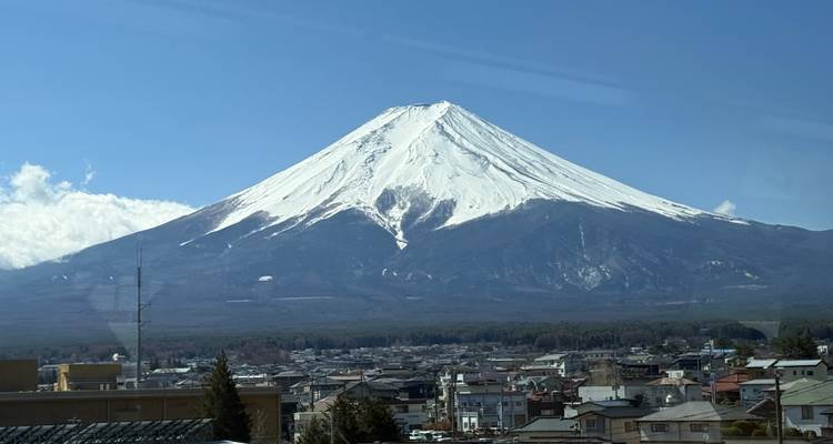 Le mont Fuji enneigé domine l'horizon au-dessus d'une ville japonaise sous un ciel bleu dégagé.