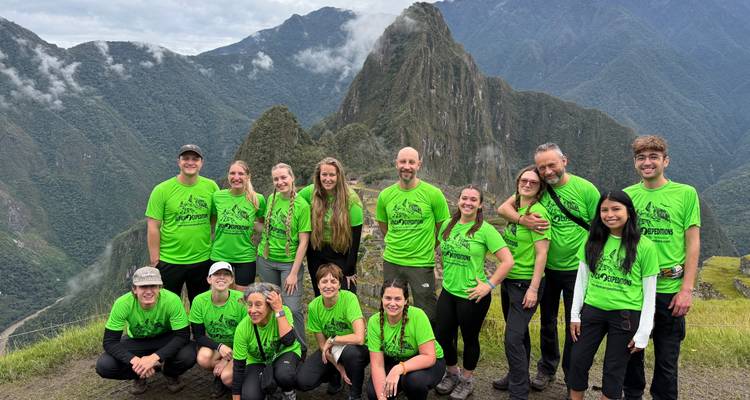 Glückliches Trekking-Team in passenden grünen Hemden posiert mit dem ikonischen Machu Picchu-Gipfel, der sich dahinter erhebt.