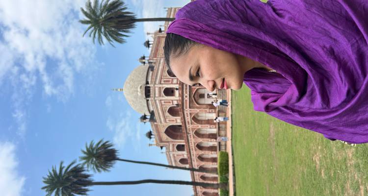 Gros plan d'une femme portant un foulard violet avec le tombeau d'Humayun et des palmiers en arrière-plan sur un ciel bleu éclatant