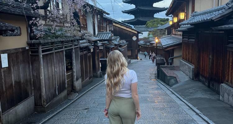 Joven mujer camina por un sendero de piedra hacia una pagoda en el distrito tradicional de Kioto al anochecer