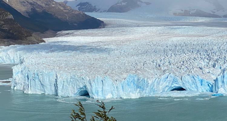 Massif mur bleu du glacier Perito Moreno rencontre les eaux turquoise du lac avec des montagnes lointaines qui se dressent.