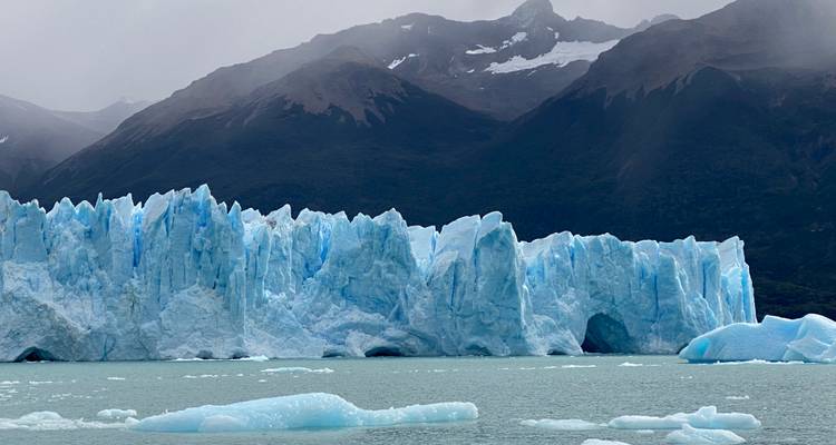 Gros plan des tours de glace bleue dentelées du glacier Perito Moreno sur fond de montagnes brumeuses.