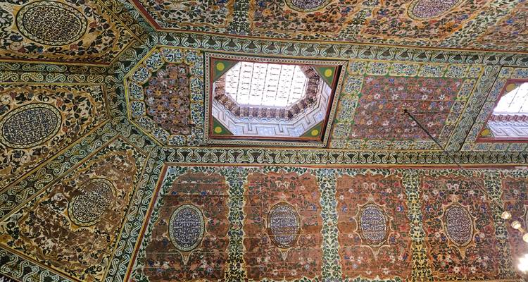 Plafond marocain très orné avec des motifs géométriques et floraux colorés autour d'un puits de lumière.