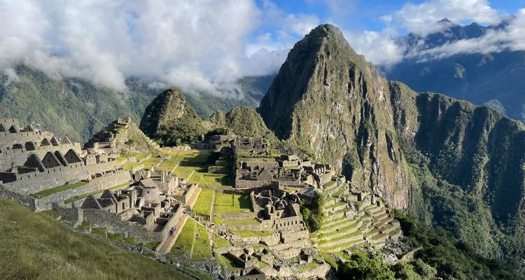 Vue aérienne emblématique de la citadelle de Machu Picchu perchée sur une crête montagneuse verdoyante entourée de sommets de forêt nuageuse.