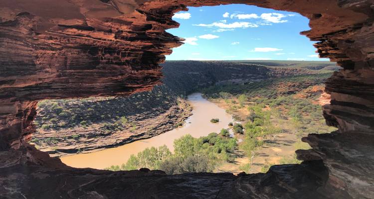 Une fenêtre rocheuse spectaculaire encadre une vallée fluviale sinueuse et un paysage de canyon accidenté sous un ciel lumineux.