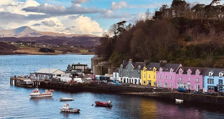 Une rangée colorée de maisons borde le front de mer de Portree avec des bateaux qui dansent dans la baie.