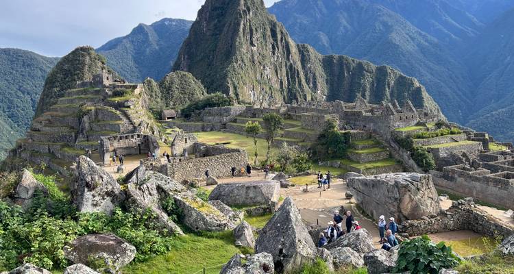 Vista panorámica de las terrazas y pico de Machu Picchu con visitantes explorando.