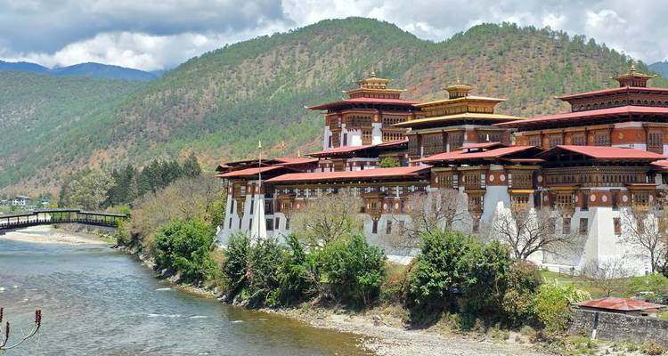 Punakha Dzong encaramado en la confluencia de dos ríos con colinas boscosas al fondo.