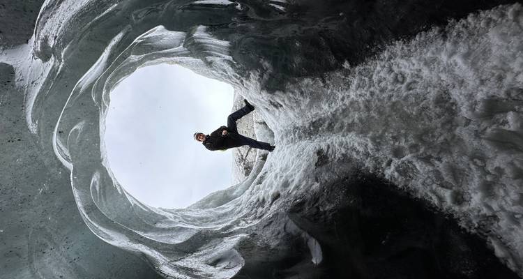 Un aventurier pose à l'intérieur d'une entrée de grotte de glace circulaire encadrée par des parois de glace bleue sculptées