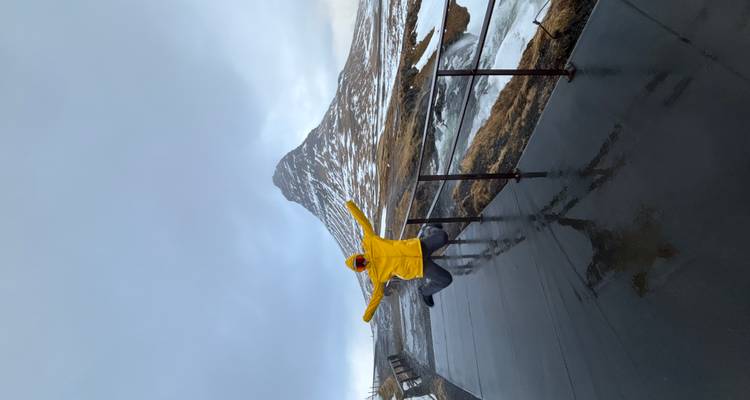 Voyageur excité en veste jaune saute de joie sur une plateforme d'observation avec la montagne enneigée Kirkjufell en arrière-plan