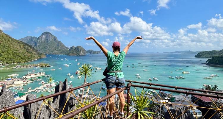 Traveler with raised arms on a viewpoint overlooking turquoise bays and limestone cliffs of El Nido.