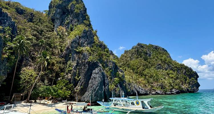 Tropical beach cove with towering karst cliffs, bangka boats and crystal clear water.