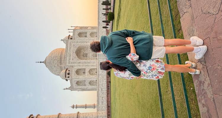 Paar umarmt sich, während es den Taj Mahal bei Sonnenuntergang bewundert und auf gepflegten Rasenflächen steht.