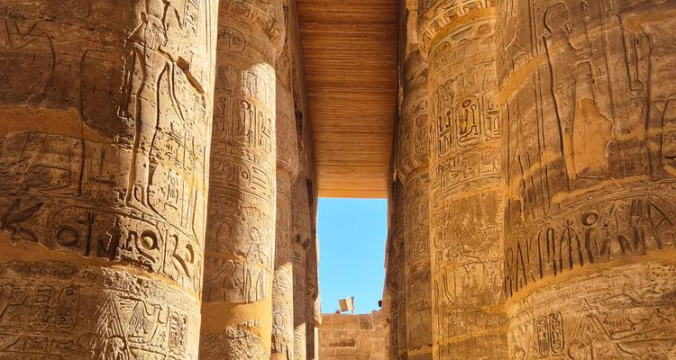 Colonnes massives de grès remplies d'hiéroglyphes dans un temple égyptien antique avec le ciel bleu encadré au-dessus.