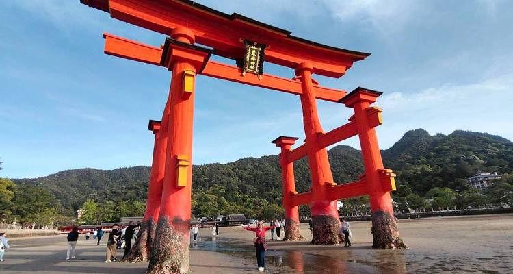 Emblématique Grand Torii vermillon de Miyajima s'élevant des vasières sableuses avec des collines boisées en arrière-plan.