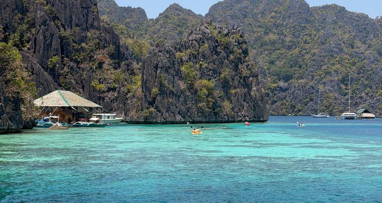 Laguna turquesa rodeada de espectaculares acantilados de piedra caliza con kayakistas y una cabaña flotante en Palawan.