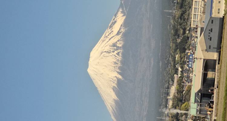 Met sneeuw bedekte berg Fuji rijst op boven een heldere blauwe lucht met een stad op de voorgrond.