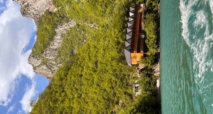 Cabaña de madera en lago turquesa rodeada por paredes empinadas de cañón verde y picos escarpados.