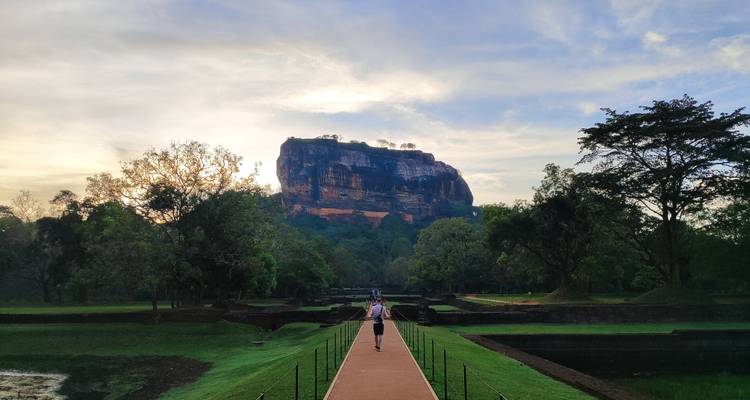 Viajero caminando por el largo sendero de ladrillos hacia la icónica fortaleza rocosa de Sigiriya bajo la luz del amanecer.