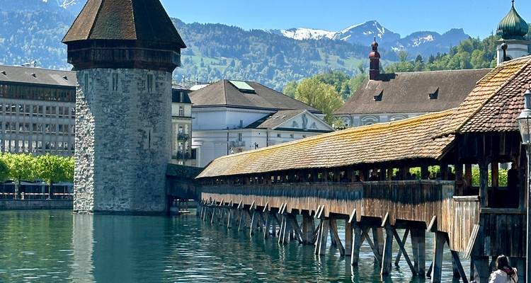 Luzerns hölzerne Kapellbrücke überspannt ruhiges blaues Wasser mit Alpengipfeln dahinter.