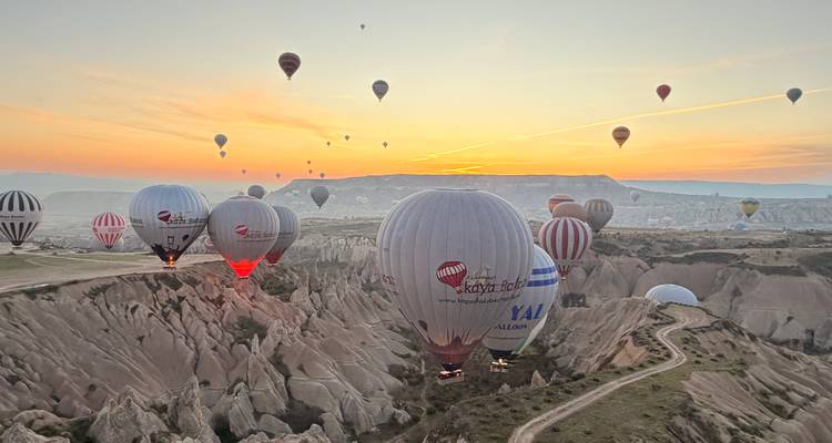 Dutzende von Heißluftballons schweben bei Sonnenaufgang über Kappadokiens zerklüftete Täler, der Himmel in sanften Orangetönen gemalt.