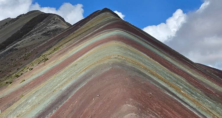 Nahaufnahme der farbenfrohen geschichteten Gesteinsschichten des Rainbow Mountain unter einem strahlend blauen Himmel.