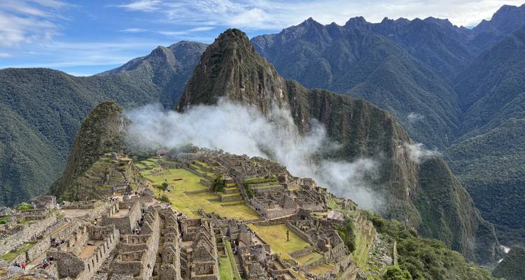 Ikonische Luftaufnahme der Zitadelle Machu Picchu mit aufsteigendem Nebel und dramatischen Andengipfeln im Hintergrund.