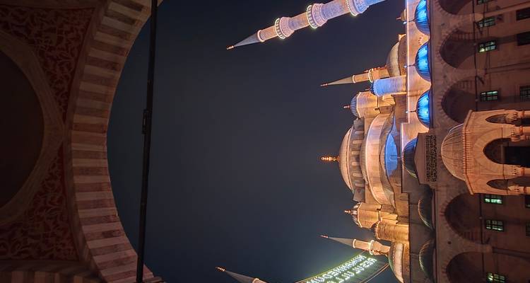 Les dômes et minarets illuminés de la Mosquée Bleue d'Istanbul brillent contre un ciel nocturne profond, encadrés par une entrée voûtée.