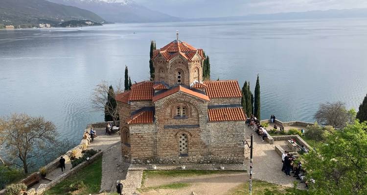Byzantijnse stenen kerk gelegen boven glinsterende meer met bergen aan de horizon.