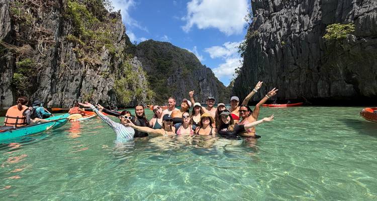 Groep vrienden poseert tot aan de taille in turquoise lagune omlijst door torenhoge kalkstenen kliffen.