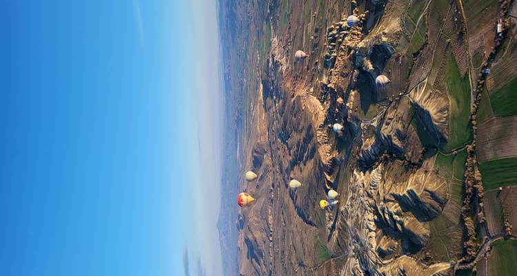 Vue aérienne panoramique des vallées de Cappadoce parsemées de montgolfières colorées au lever du soleil.