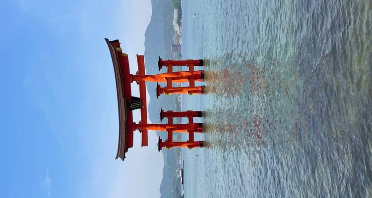 Levendige rode torii-poort van Itsukushima-heiligdom staand in kalm blauw water met verre heuvels onder een heldere hemel