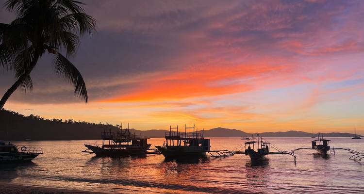 Magnifique coucher de soleil tropical avec des bateaux amarrés silhouettés contre des nuages colorés et une eau calme