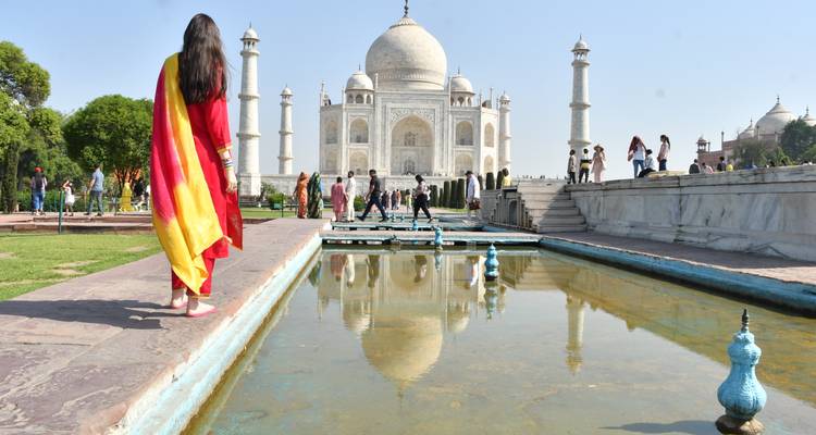 Le Taj Mahal emblématique se reflète dans un long bassin tandis que les visiteurs explorent la terrasse de marbre.