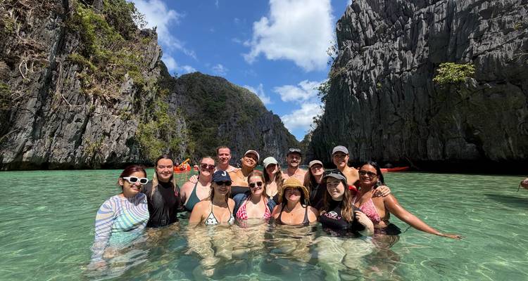 Groupe de nageurs posant dans une eau turquoise cristalline encadrée par des falaises de calcaire imposantes sous un ciel bleu.