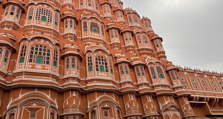 Close-up of the ornate red and pink façade of Jaipur’s Hawa Mahal with green windows under cloudy skies.