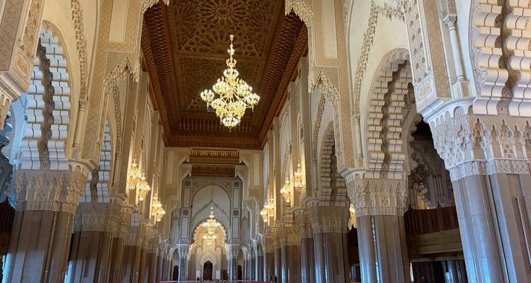 Vaste hall intérieur du mausolée Hassan II illuminé par un grand lustre, avec des arches ornées et un plafond à motifs.