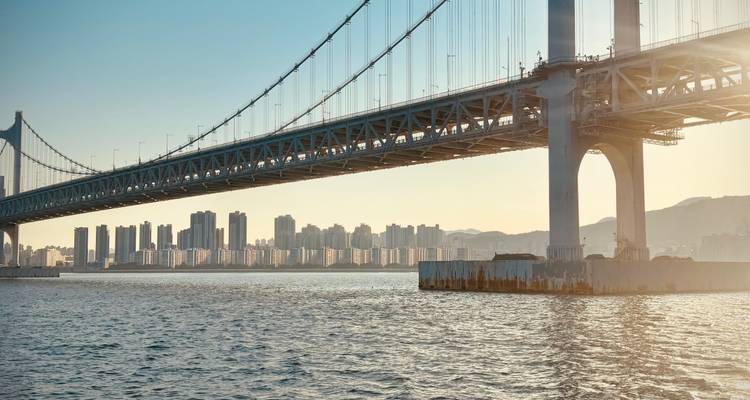 Puente colgante de Gwangan extendiéndose sobre el agua en la hora dorada con el horizonte de Busan de fondo
