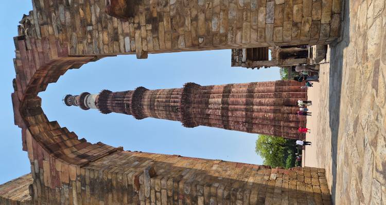 Le majestueux Qutub Minar encadré par une arche de pierre avec des visiteurs qui se promènent à sa base.