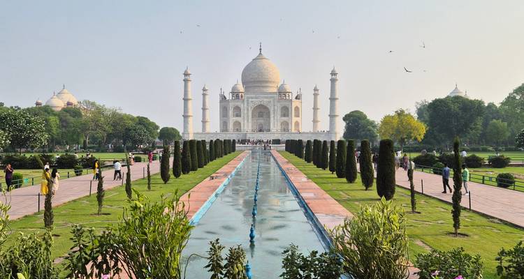 Vue classique de face des jardins du Taj Mahal avec bassin de réflexion et visiteurs sur les chemins.